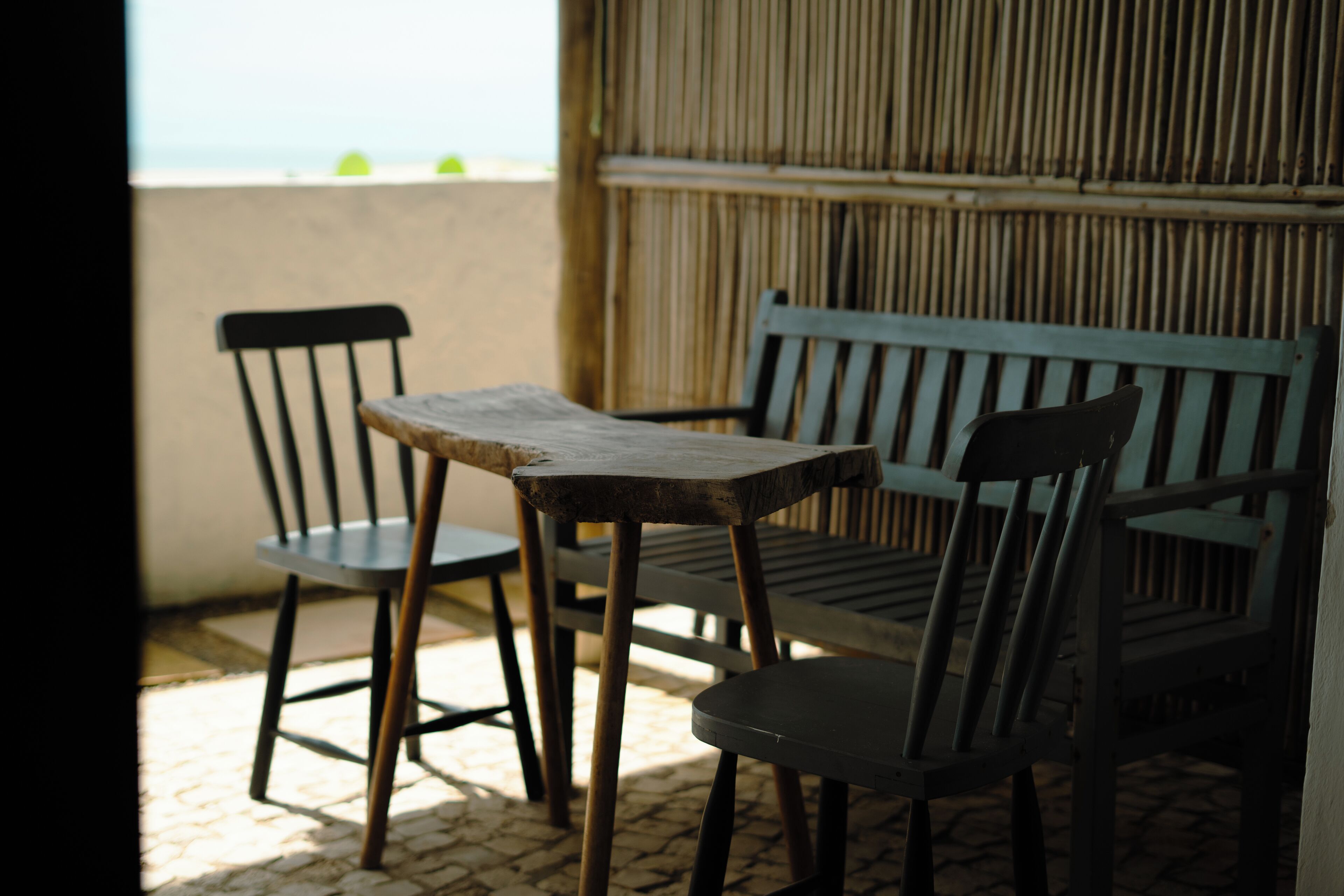 A wooden table and two chairs on a balcony with a bamboo wall in the background.