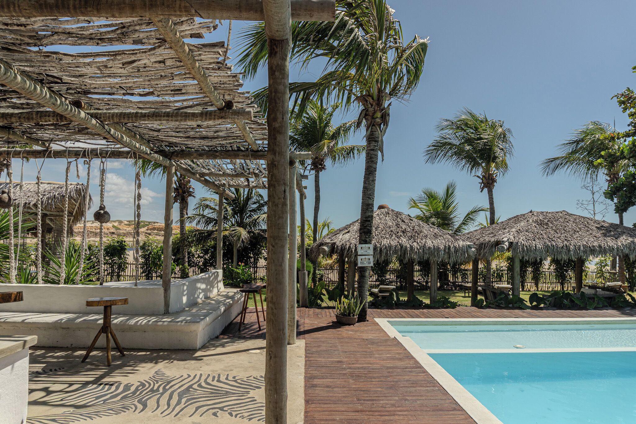 Een zwembadgedeelte met rieten parasols, palmbomen en een houten terras.