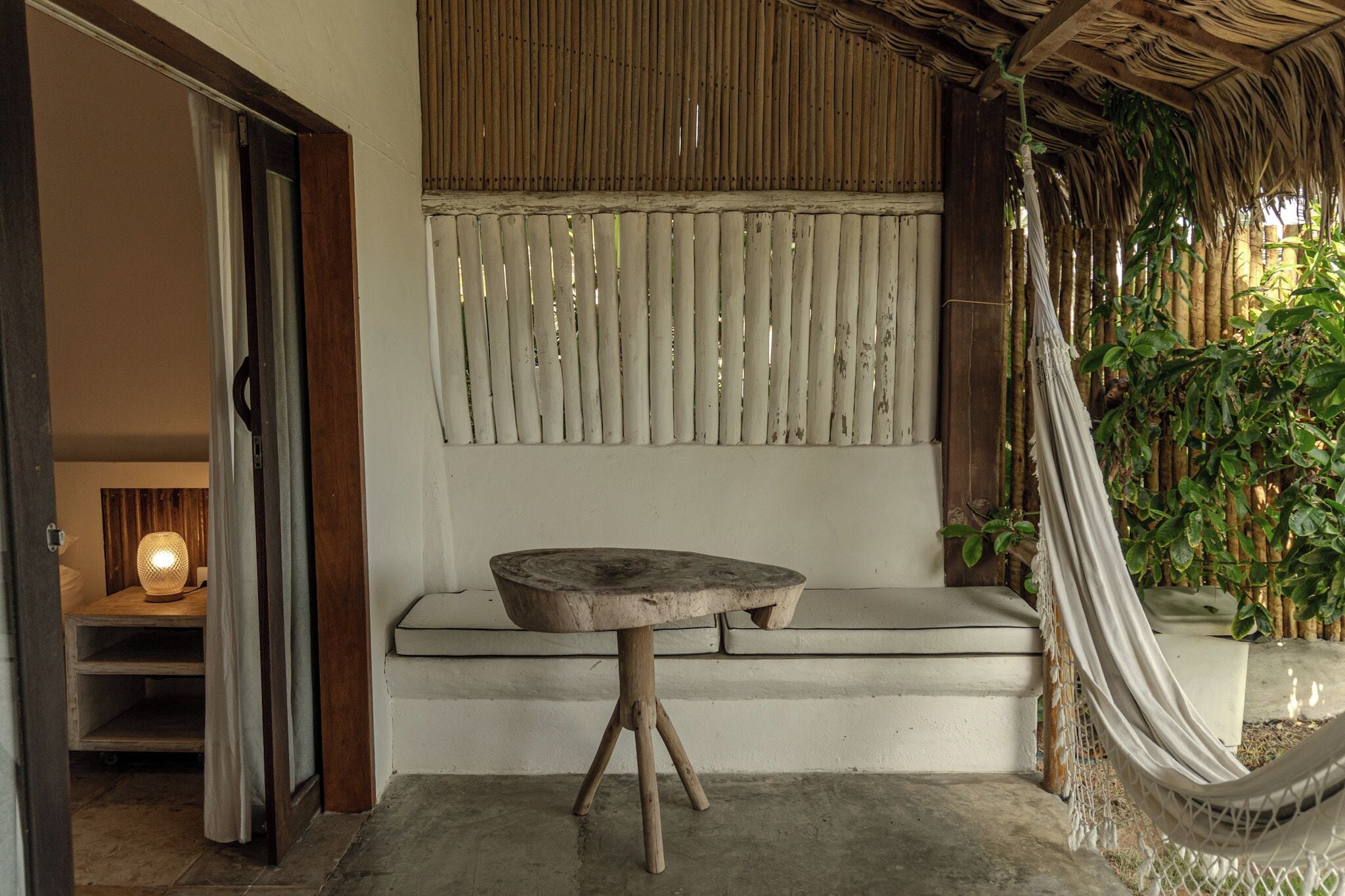 Una habitación con una mesa de madera, un banco, una hamaca y un muro de bambú.