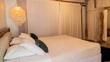 Uma cama grande com roupa de cama branca, um candeeiro pendente e uma cabeceira de madeira.