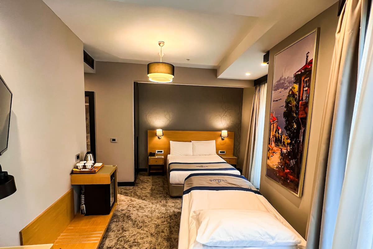 A hotel room with a bed, bedside tables, a TV, a small table, and a painting on the wall.