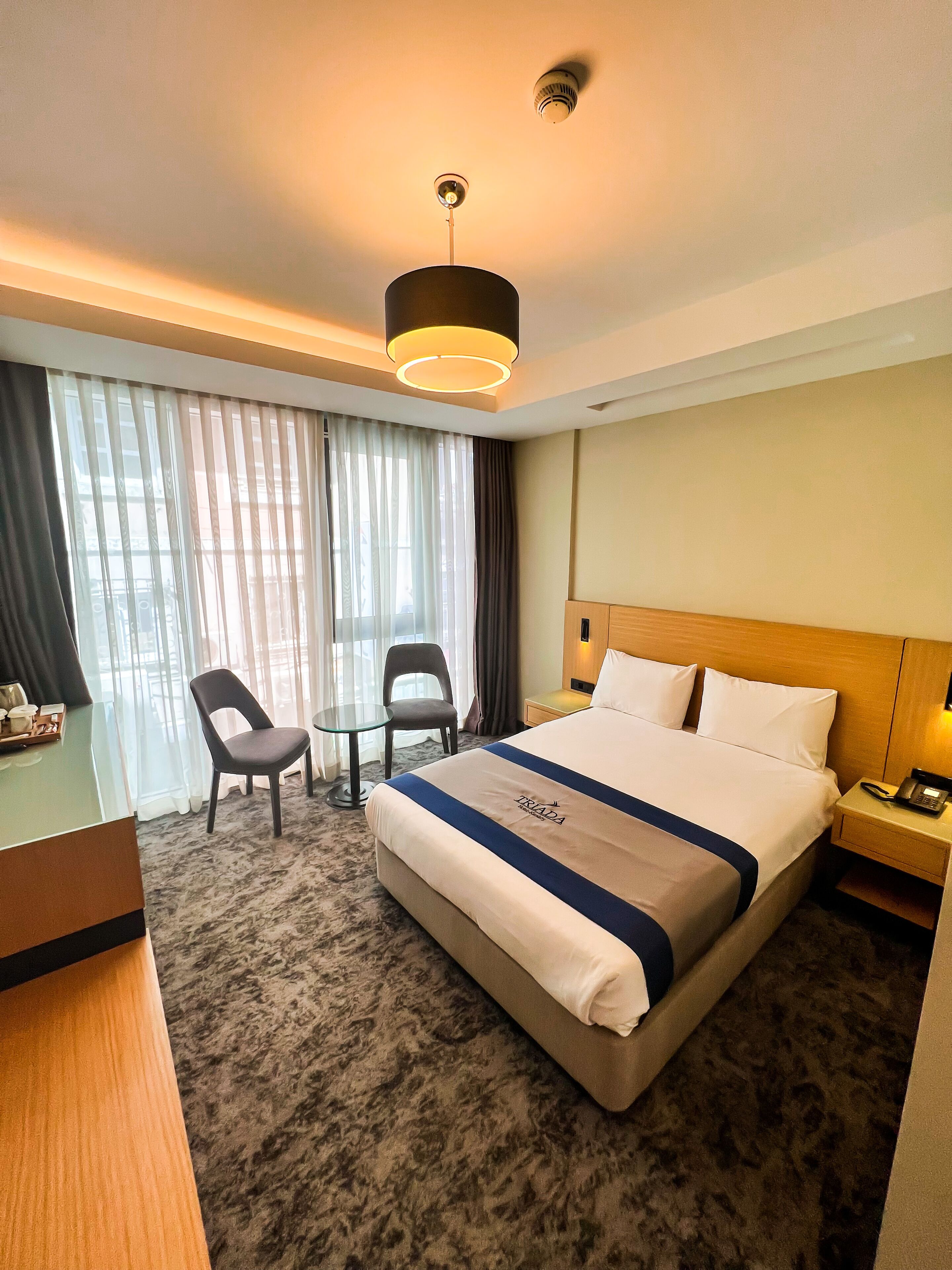 A hotel room with a large bed, a desk, two chairs, a small table, and a nightstand with a phone.