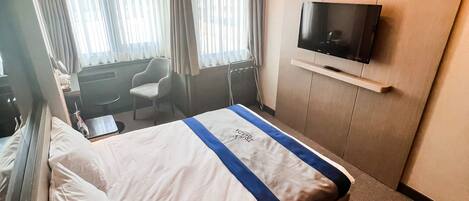 Habitación de hotel con cama, televisión montada en la pared, escritorio y silla.