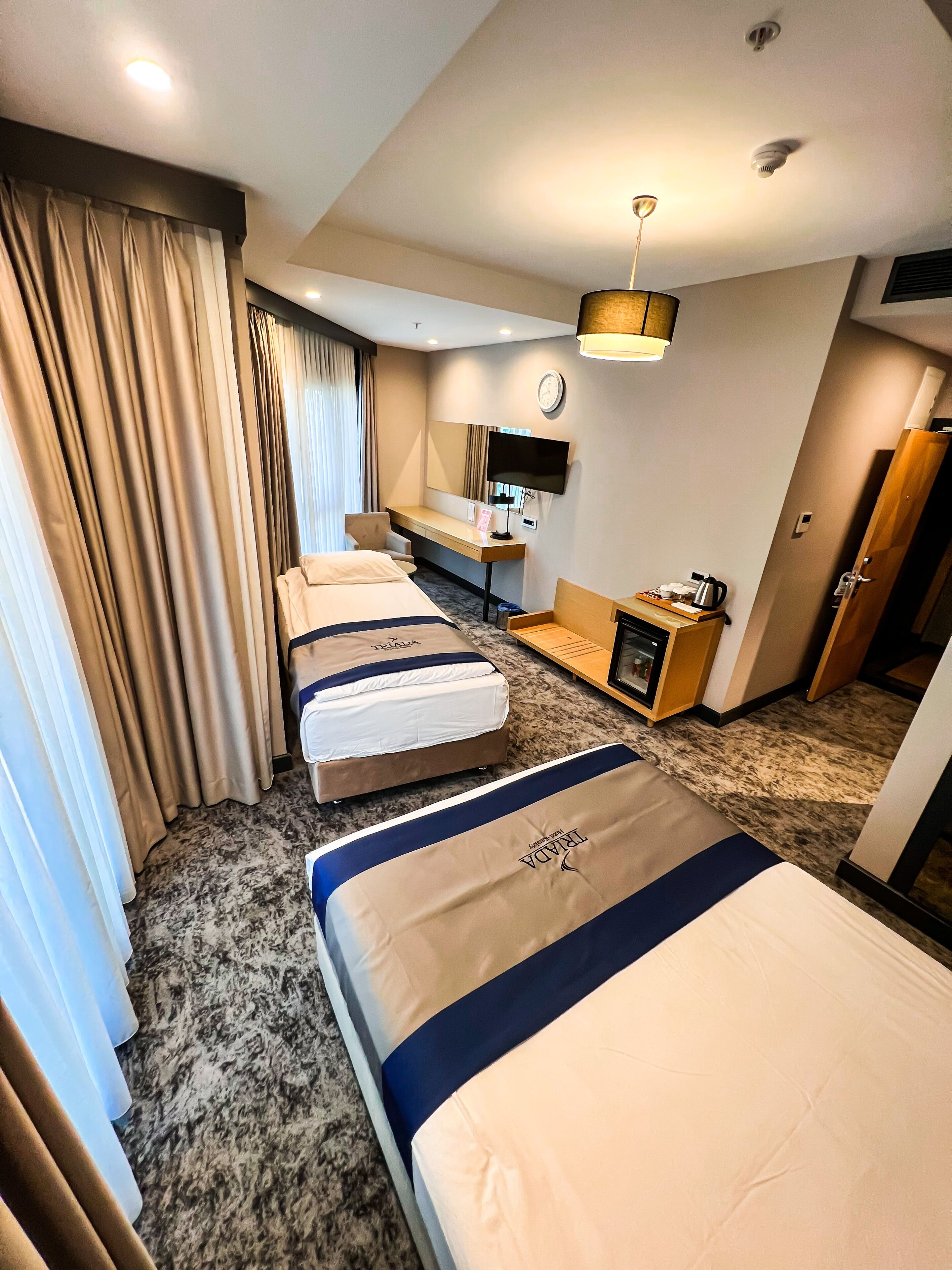 Une chambre d’hôtel avec quatre lits, un bureau, une télévision et une horloge au mur.