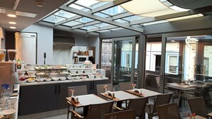 Un restaurant moderne doté d’une salle à manger avec de grandes baies vitrées, d’un buffet proposant une variété de plats et d’une cuisine située à l’arrière.
