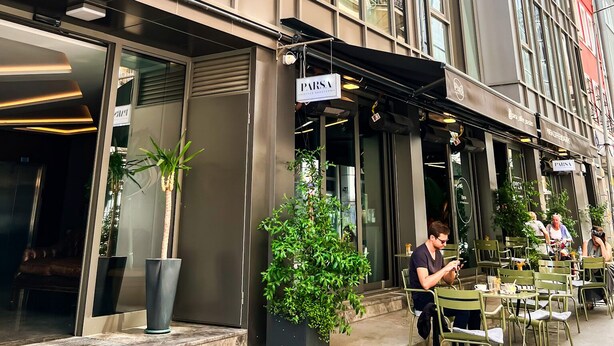Un hôtel moderne doté d’une façade en verre, d’un espace extérieur aménagé et d’un restaurant bien visible appelé PARSA.