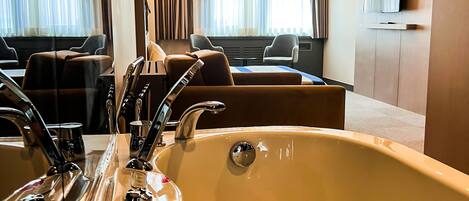 Une salle de bain d’hôtel dotée d’une grande baignoire, d’un lavabo avec plusieurs robinets et d’un téléviseur fixé au mur.