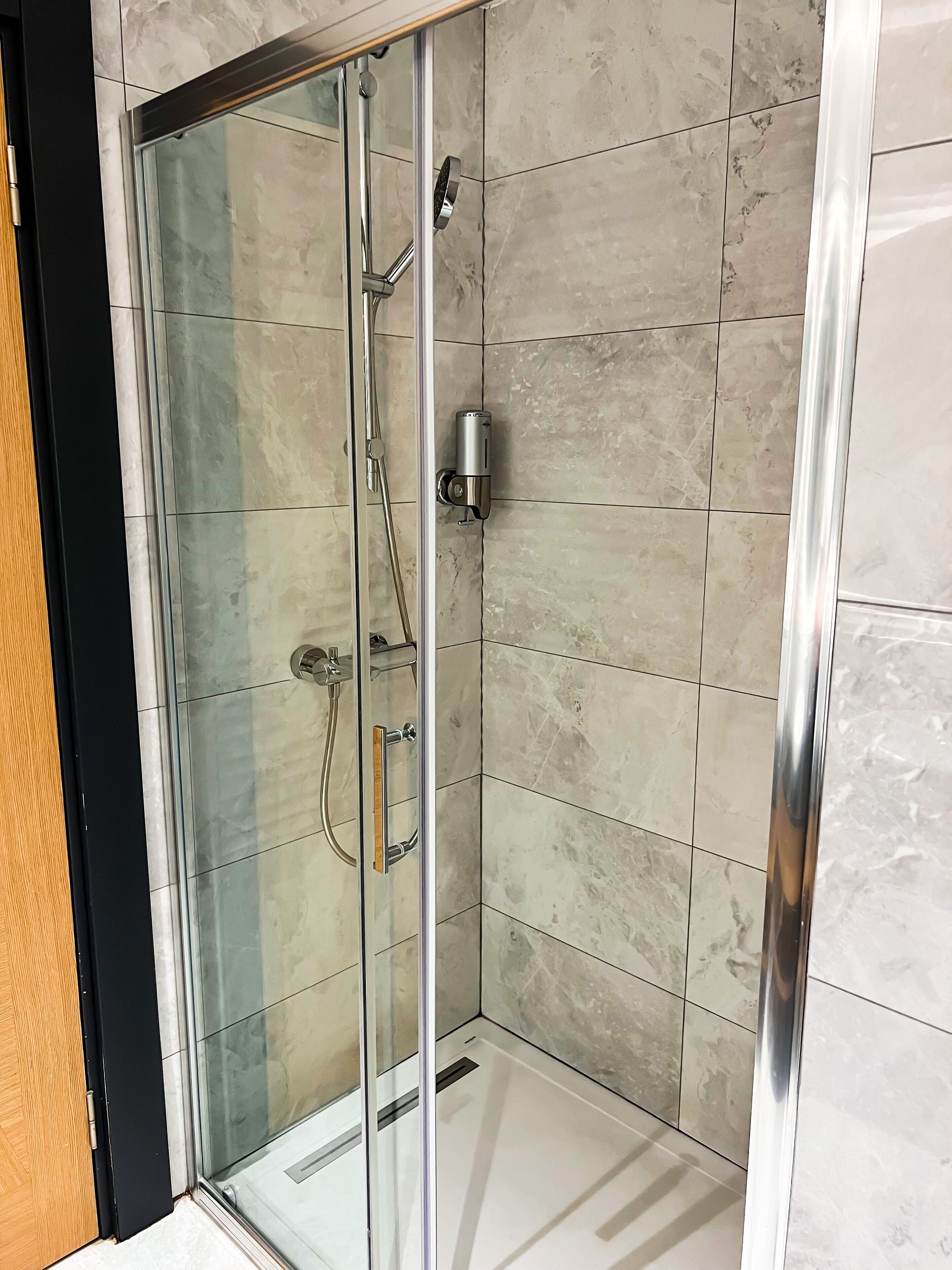 A glass-enclosed shower with a handheld showerhead and a wall-mounted faucet.