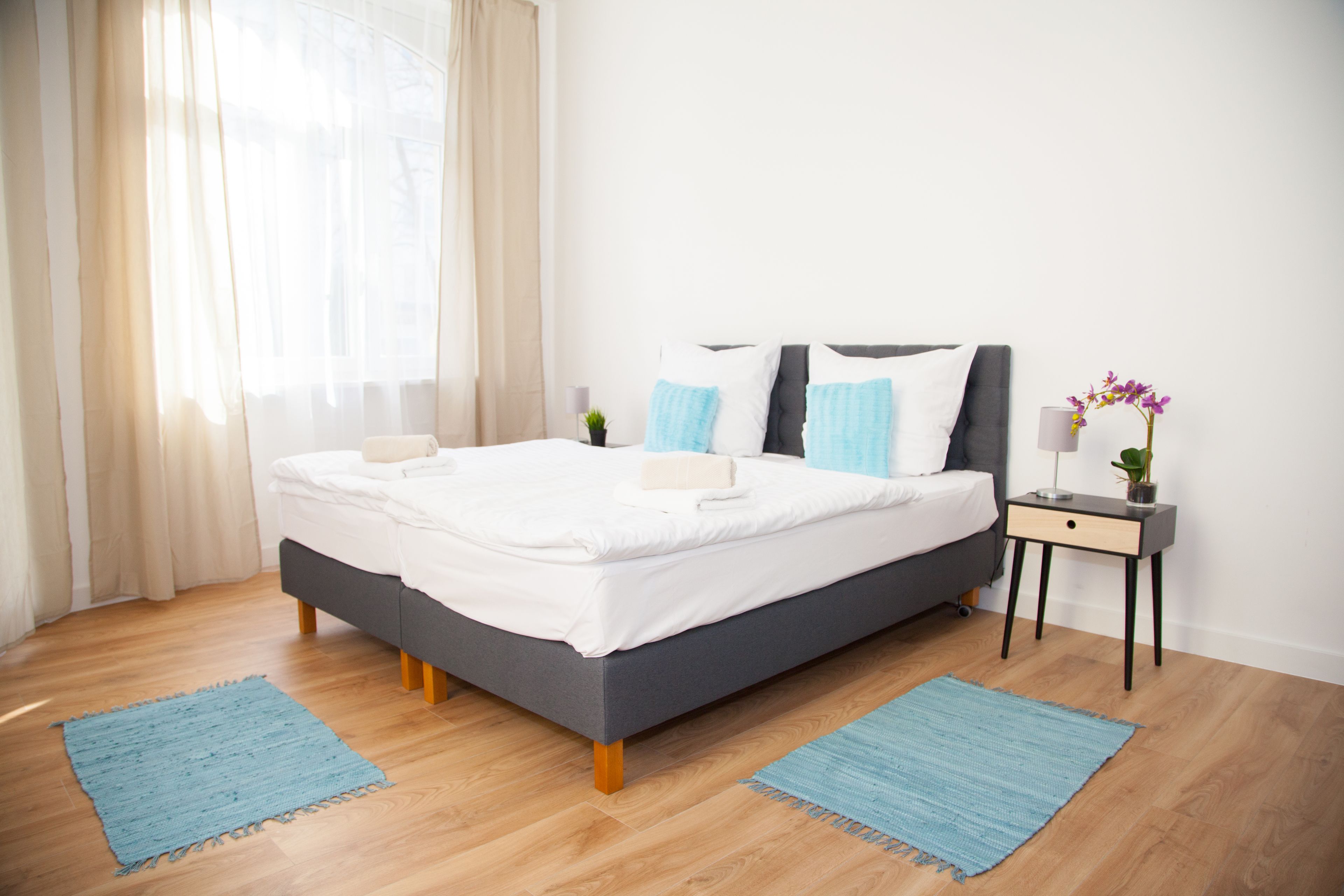 A modern bedroom with a large bed, a bedside table with a lamp, and a window with curtains.