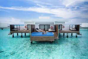An overwater villa with a pool, lounge chairs, and a private cabana.