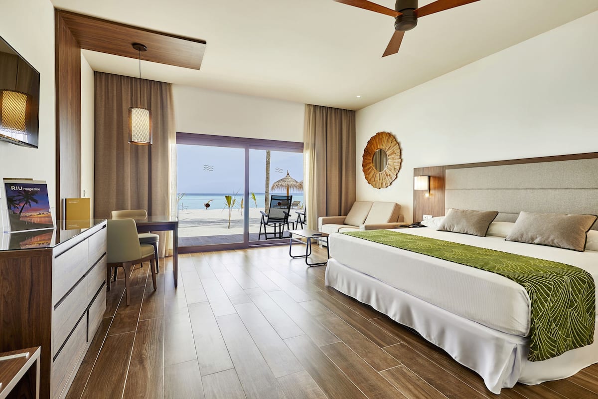 Habitación de hotel con una cama grande, un escritorio y una silla. Se ve la playa desde la ventana.
