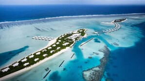 Oversigtsbillede af et resort med en lang strand, klart blåt vand og en lille ø med en anløbsbro.