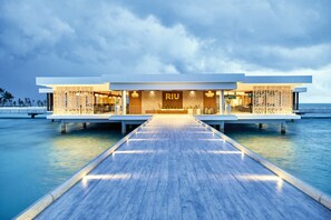 A modern hotel with a wooden deck leading to the entrance, overwater structure, and a clear view of the ocean. - Hotel Riu Palace Maldivas - All inclusive (Kedhigandu)