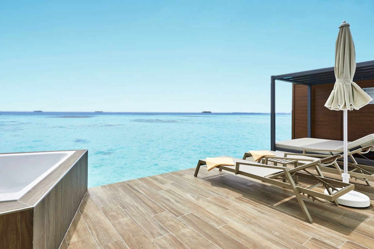 Zona junto a la piscina con sillones de descanso y jacuzzi, con vistas a un mar azul y transparente.