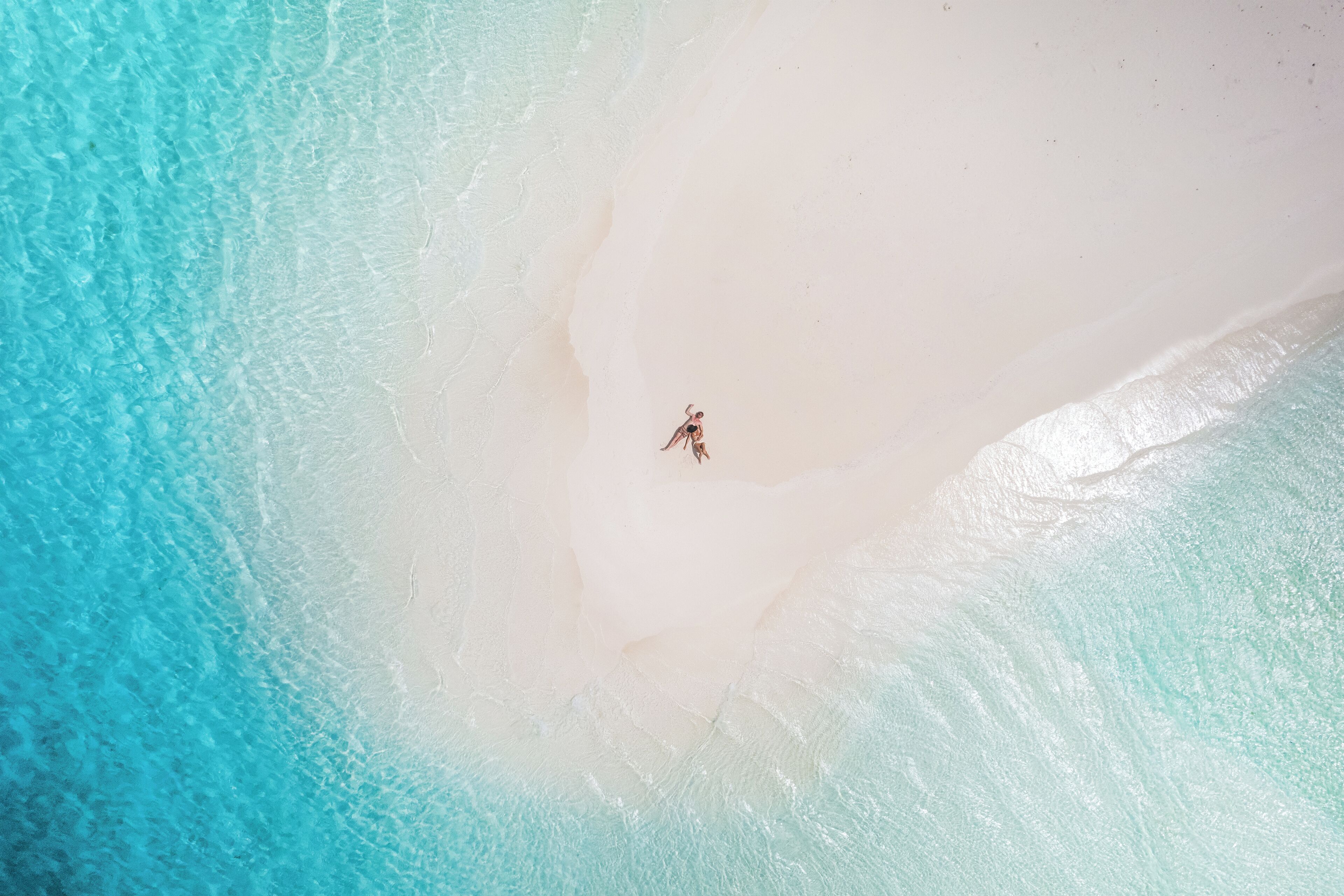 Luchtbeeld van een strand met helder turquoise water en wit zand.