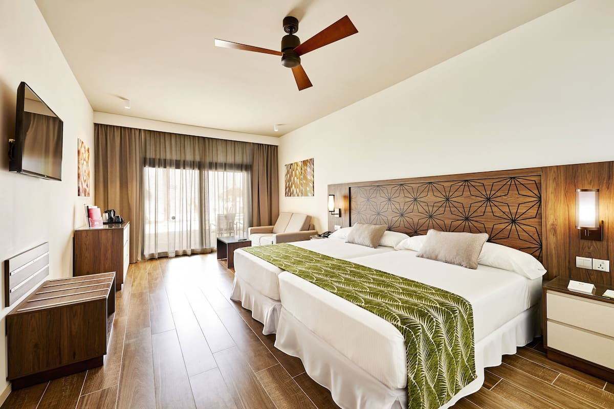 A hotel room with a large bed, a desk, a chair, a ceiling fan, and a TV on the wall.
