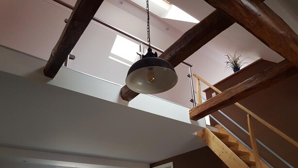 Een kamer in loftstijl met dakraam, houten balken, een trap en een rode stoel.