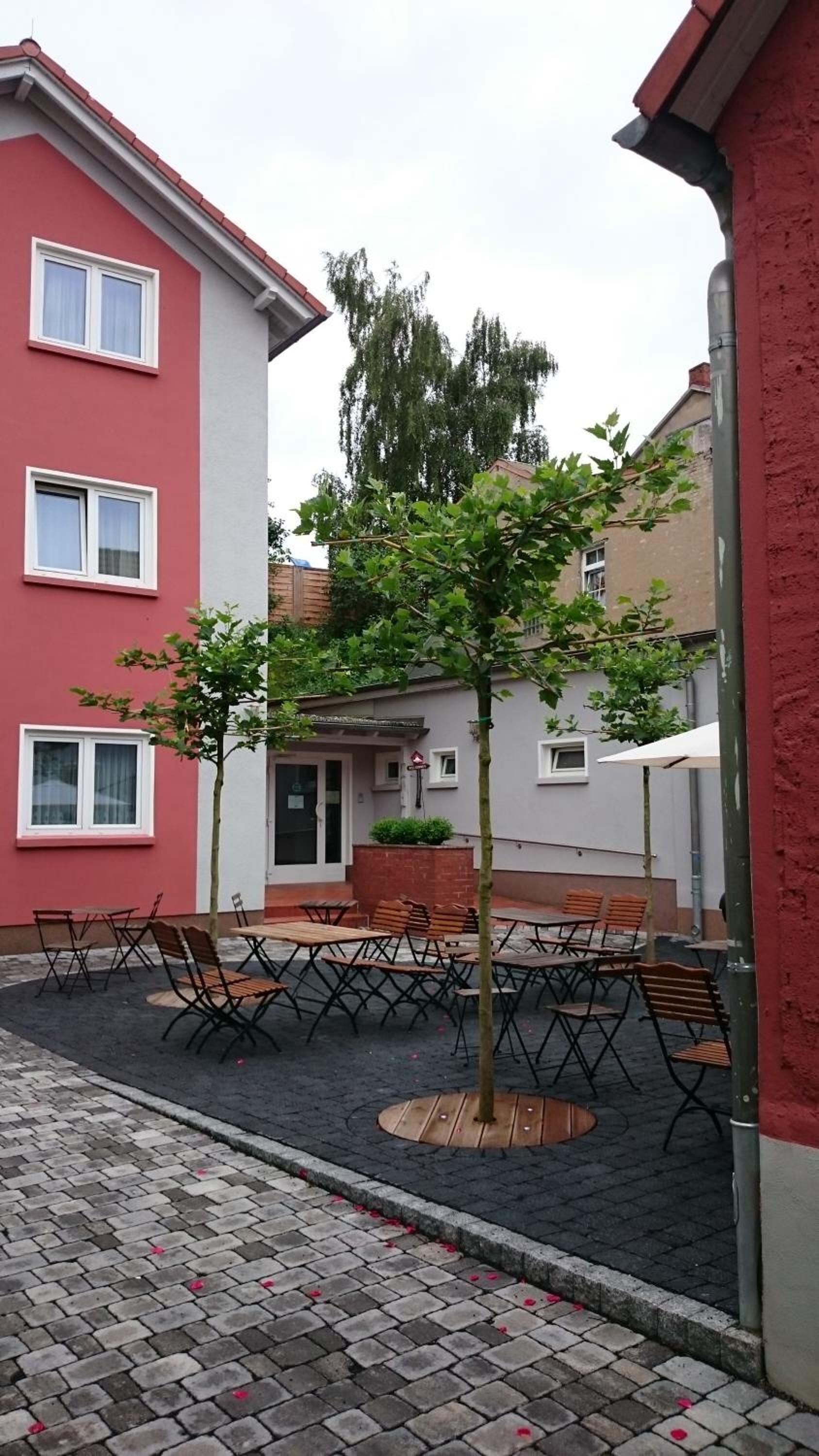 A courtyard with outdoor seating, a tree, and a building with red and white walls.