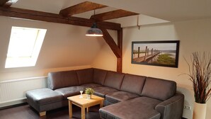 Een moderne woonkamer met een hoekbank, een klein houten bijzettafeltje en een potplant.