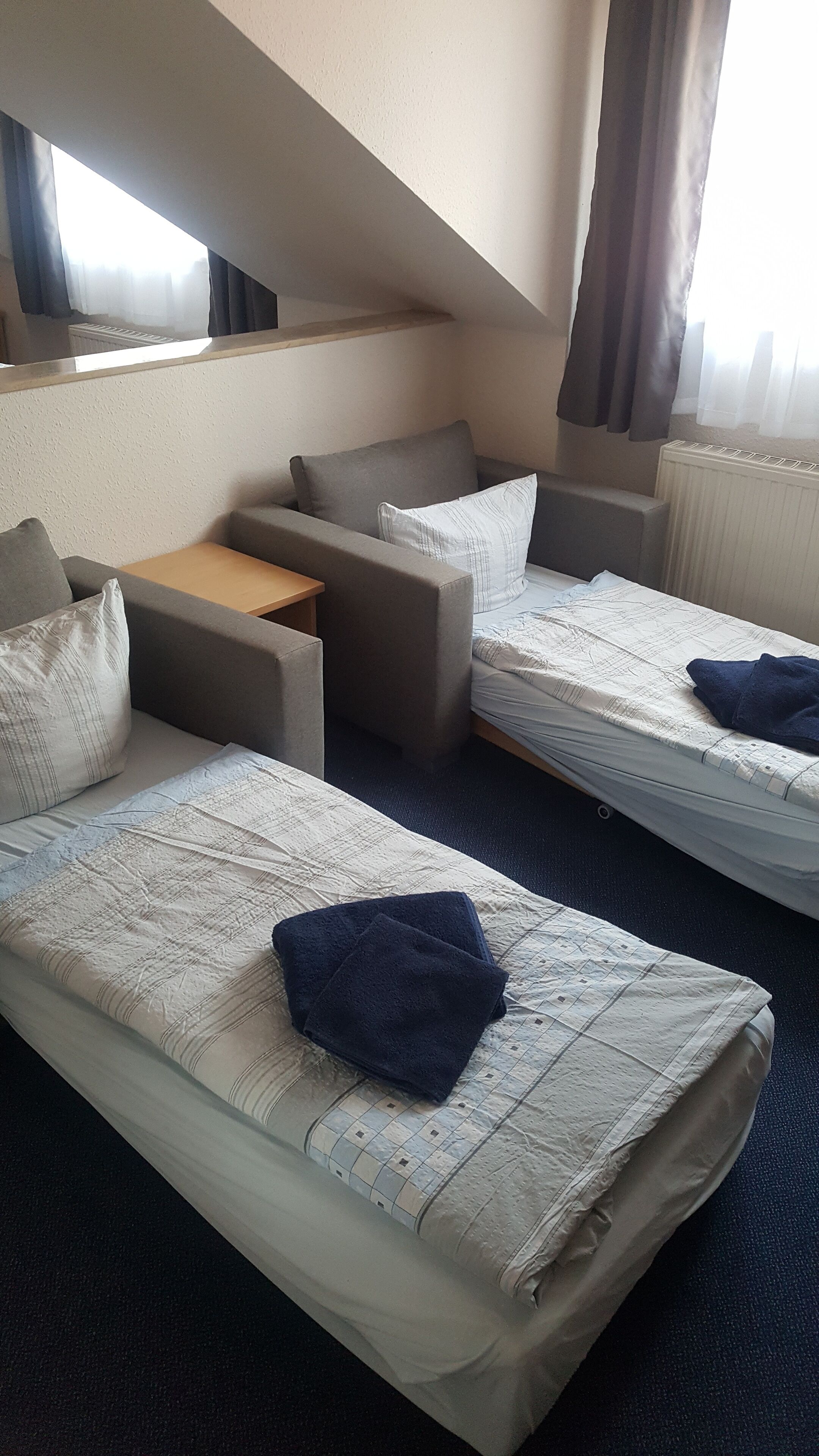 A hotel room with two single beds, a sofa, a small table, and a window with curtains.