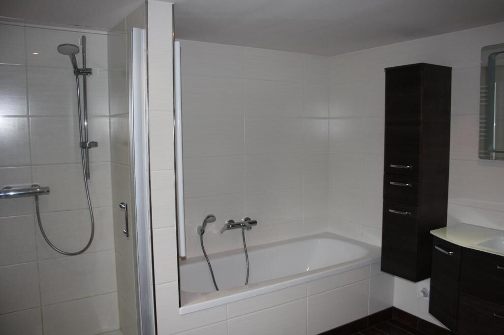 A modern bathroom with a glass-enclosed shower, a standalone bathtub, and dark wooden cabinets.