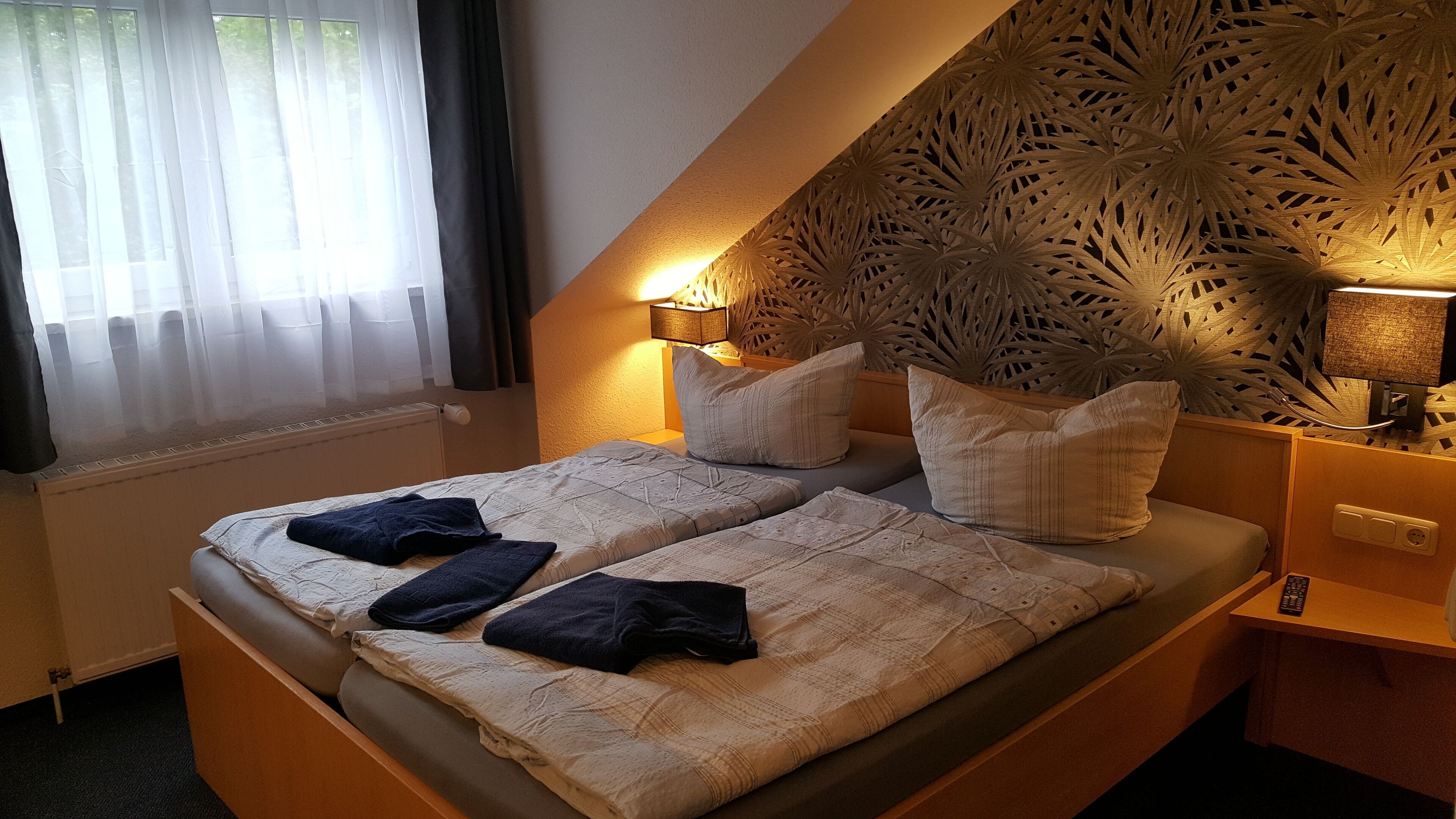 A twin bed with two pillows, a bedside table with a lamp, and a decorative wall panel.