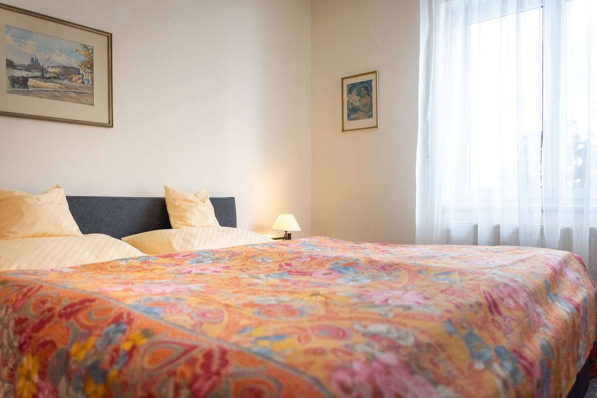 Habitación de hotel con una cama, una mesita de noche con lámpara y dos cuadros en la pared.