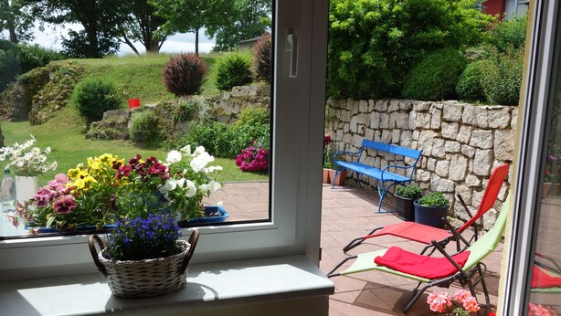 A window with a view of a stone wall, a bench, and a basket of flowers. - Ferienwohnung Schloss Schönberg (Bad Brambach)