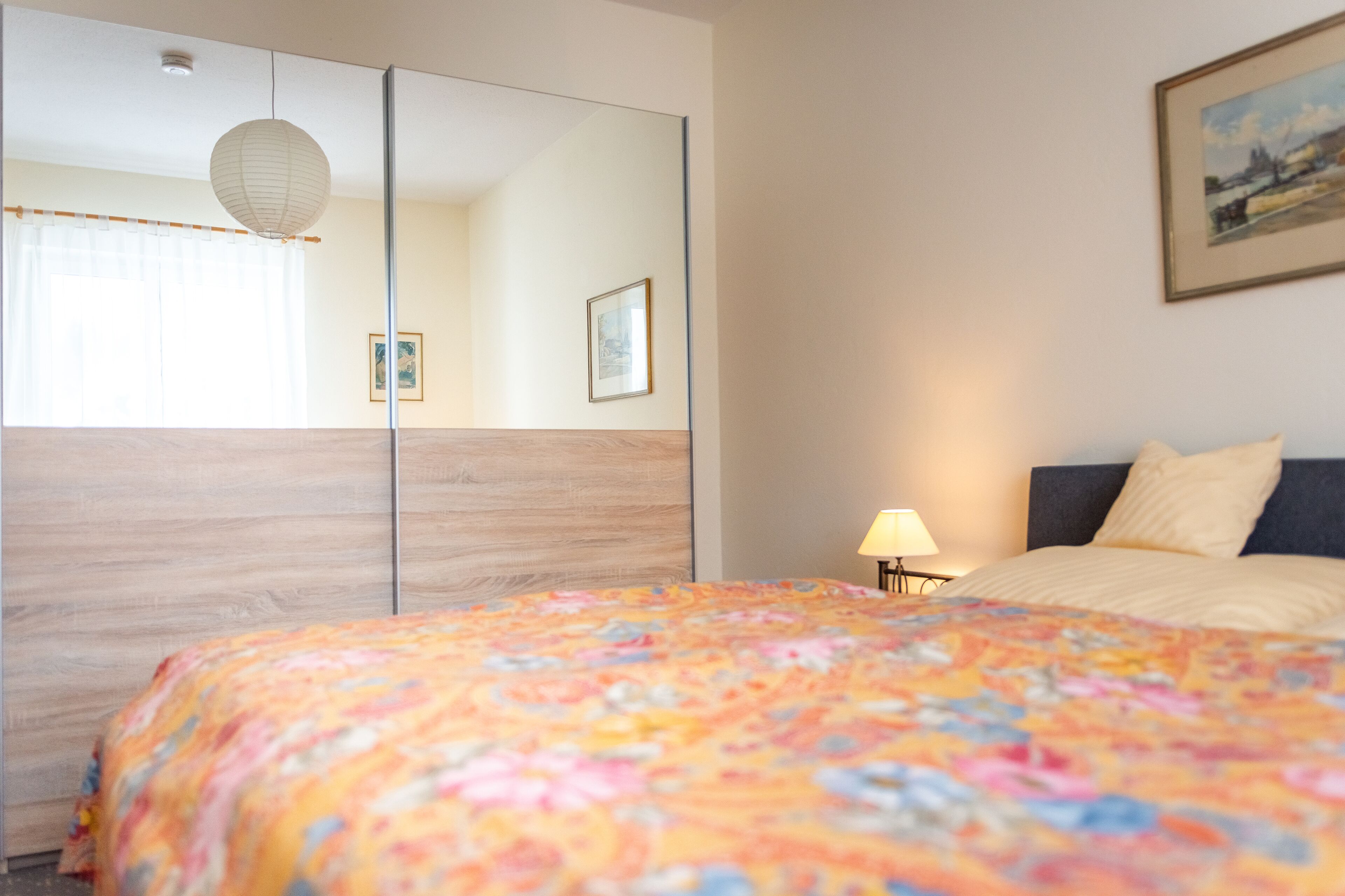 A hotel room with a bed, a nightstand, a lamp, a mirror, and a painting on the wall.