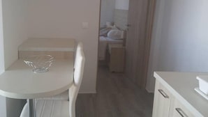 A small, compact room with a kitchenette, a dining table with a chair, and a bed in the background. - Nianthy Apartments (Rhodes)