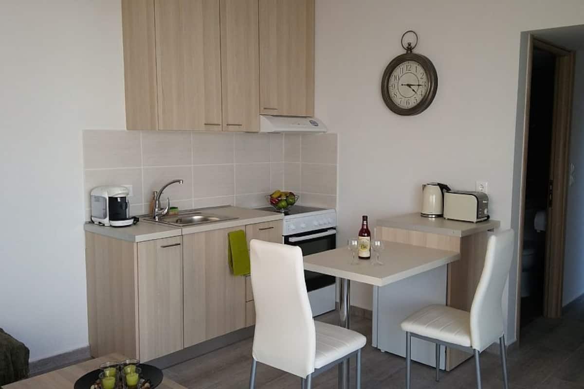 Une cuisine compacte équipée d’un évier, d’une cuisinière et d’un coin repas avec deux chaises. Une horloge est fixée au mur.