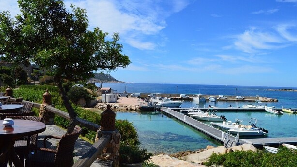 Un puerto deportivo con barcos amarrados, una terraza de madera con mesas y sillas, y vista al mar.