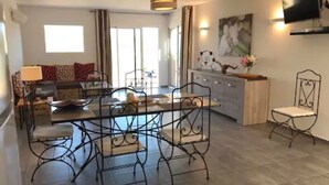 Una sala moderna con comedor, un sofá, un televisor montado en la pared y una cocina con encimera y armarios.