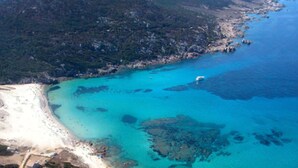 Vista aérea de una zona costera con una playa de arena, aguas turquesas cristalinas y afloramientos rocosos.