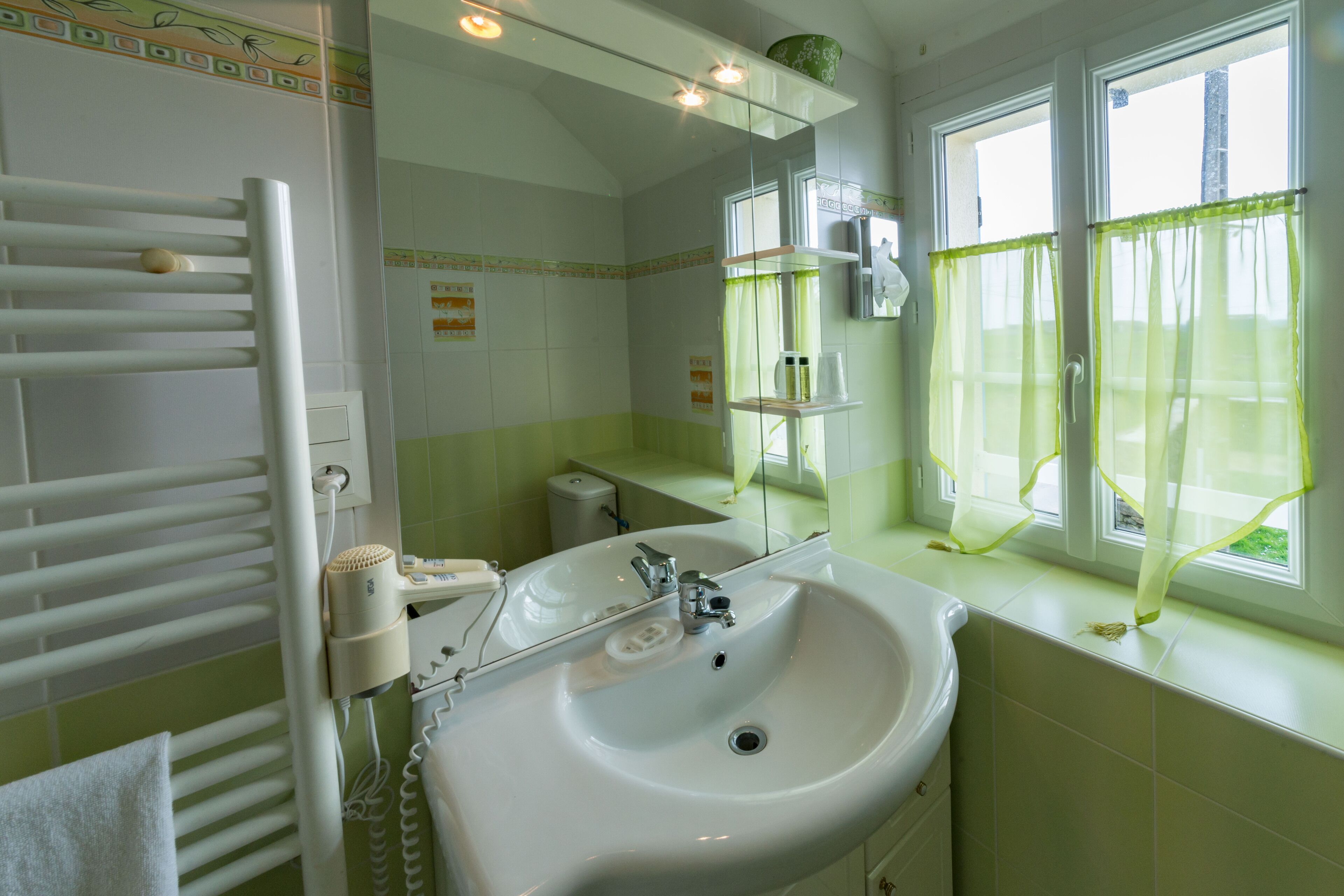 Un baño con un lavamanos blanco, un perchero, un espejo y una ventana con cortinas amarillas.