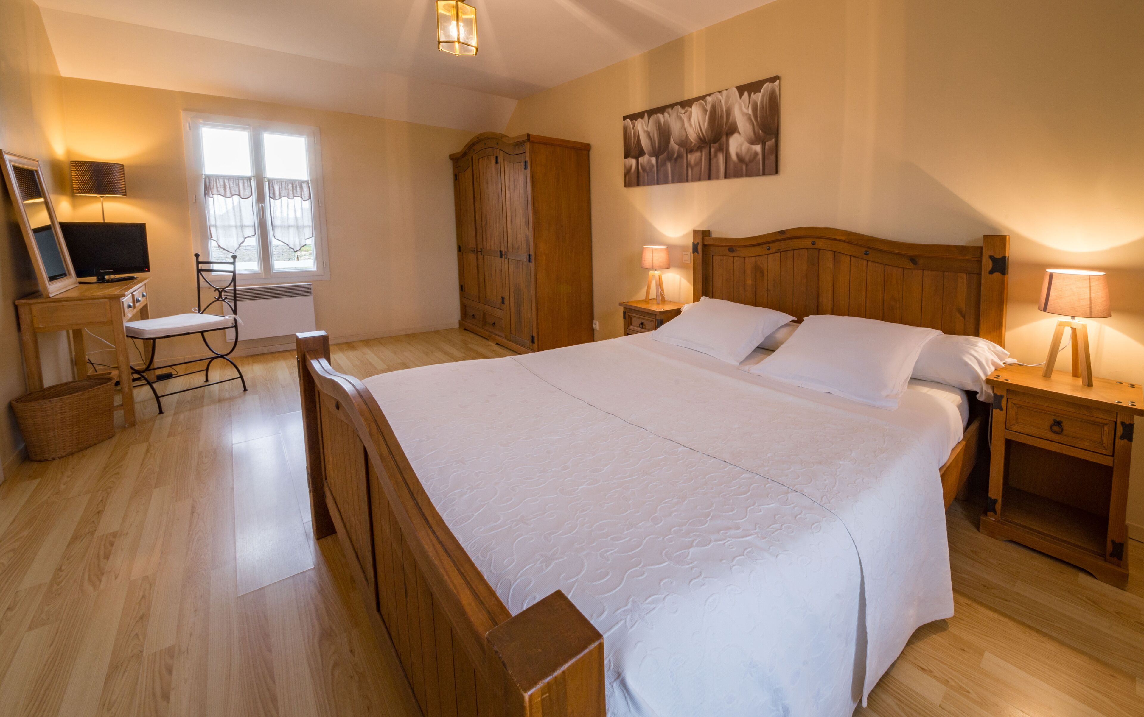 A bedroom with a large bed, wooden furniture, a desk, a chair, and a television.