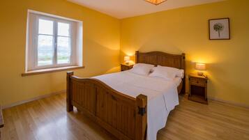 A bedroom with a wooden bed, two bedside tables with lamps, a window with a view, and a framed picture on the wall.