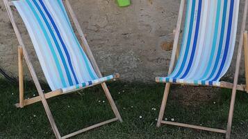Deux chaises de plage à rayures, avec une structure en bois et un siège en tissu, sont placées sur l’herbe, adossées à un mur sur lequel est posé un pot de fleurs.