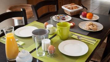 Una mesa de desayuno con platos, una taza, un vaso de jugo de naranja, una cesta de pan y un plato con galletas.