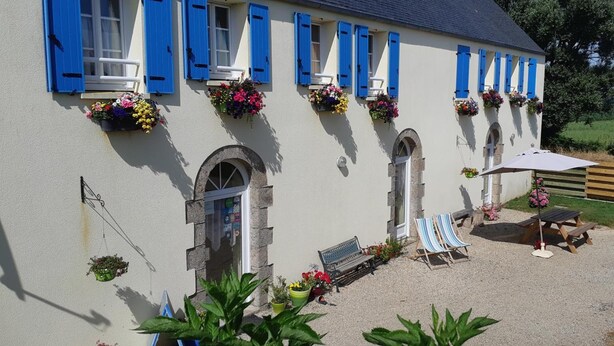 Un bâtiment avec des volets bleus, des jardinières, un banc et une table avec une chaise.