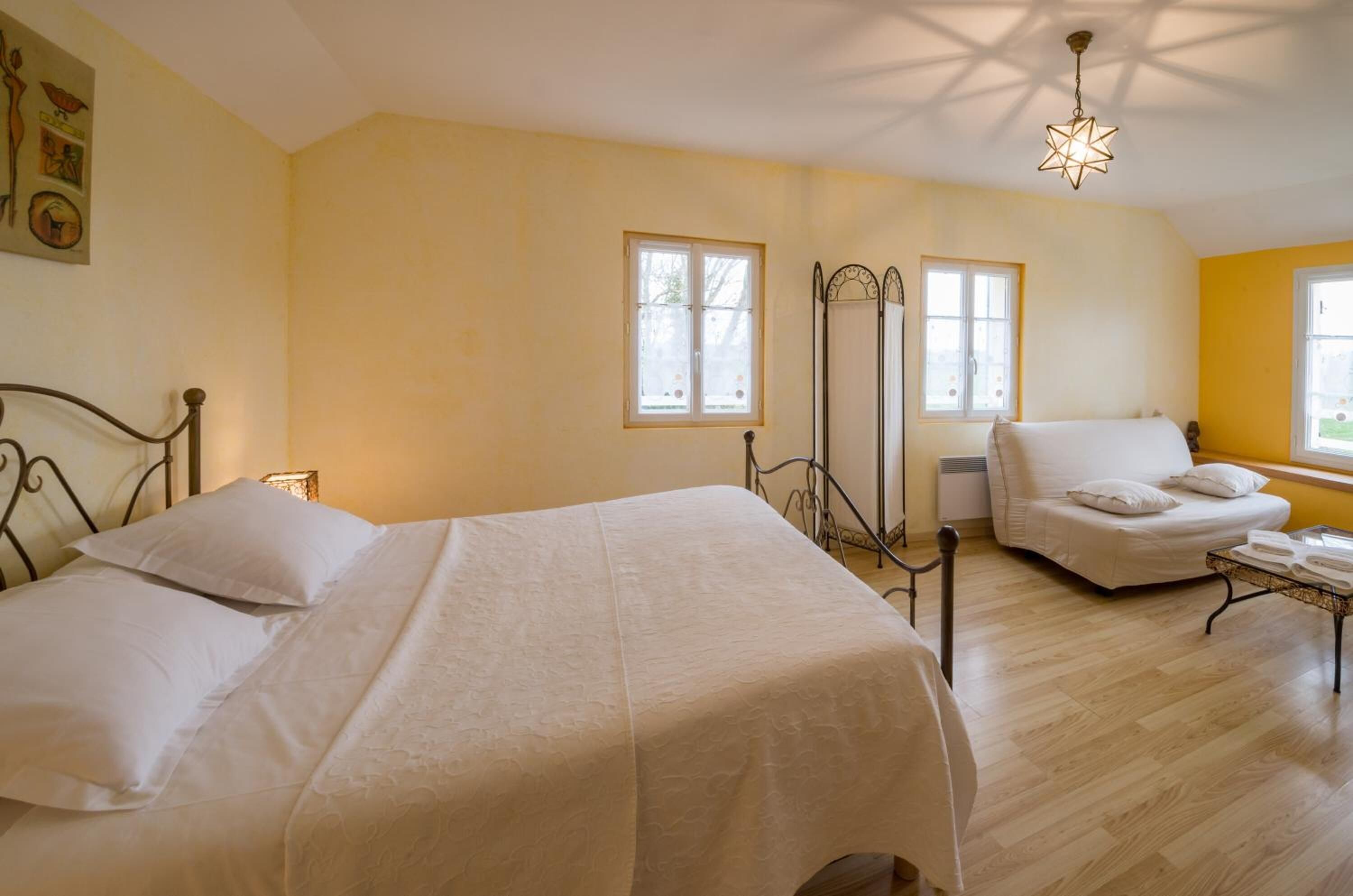 Un dormitorio con cama, una silla, una mesita y un ventanal.