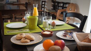 Une table de petit-déjeuner avec des assiettes remplies de nourriture, un verre de jus d’orange et un panier de pain.