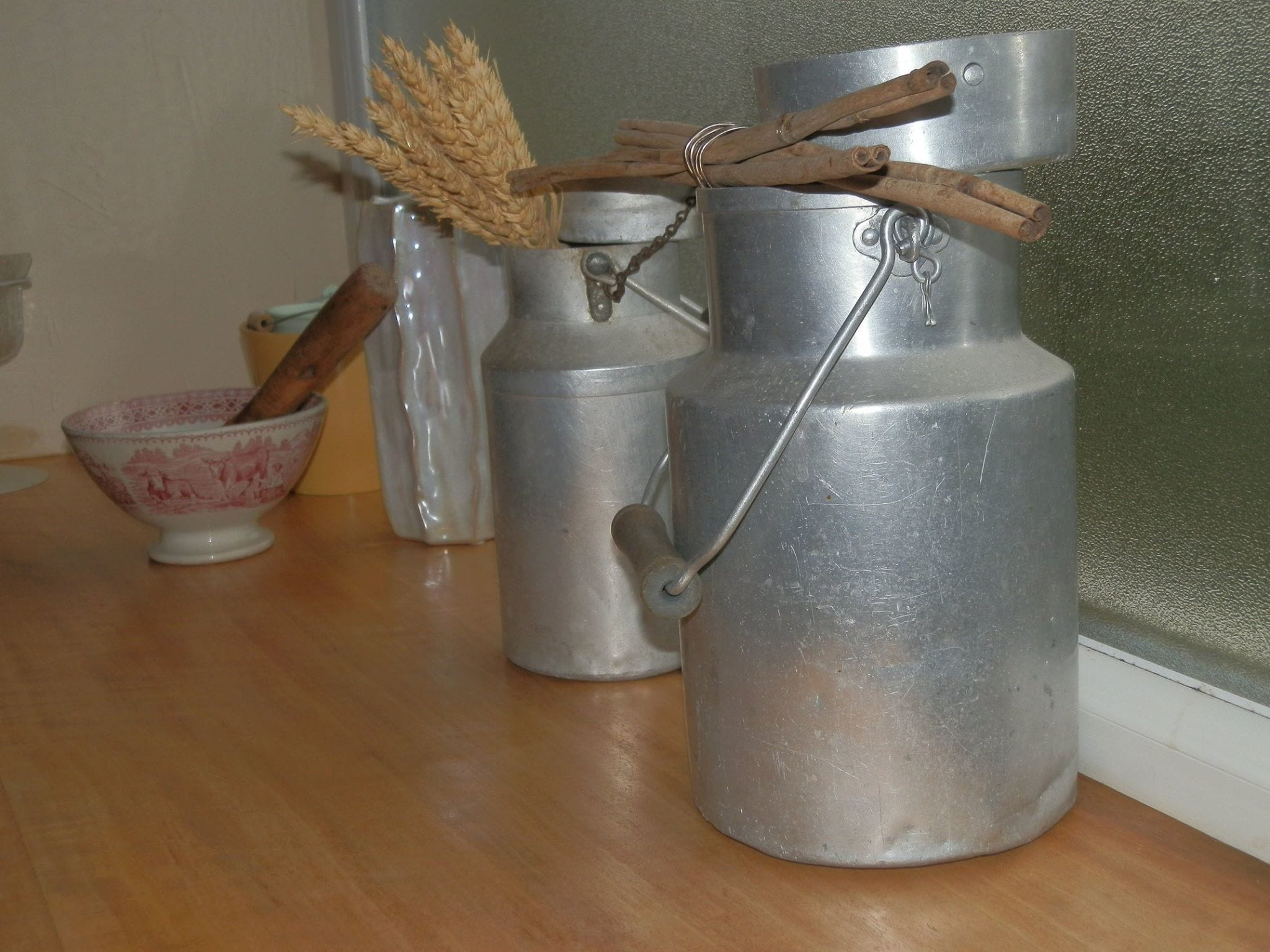A kitchen with stainless steel appliances, a wooden spoon in a bowl, and a rustic decoration with wheat stalks and cinnamon sticks.