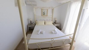 Un lit à baldaquin avec du linge de lit et des serviettes blanches, deux tables de chevet avec des lampes et un tableau encadré au mur.