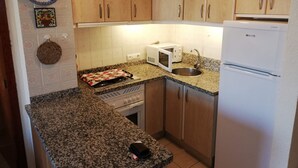 A compact kitchen with wooden cabinets, a microwave, a stove, and a refrigerator. - Infante E8-7º Solo Familias! (Playa de Gandía)