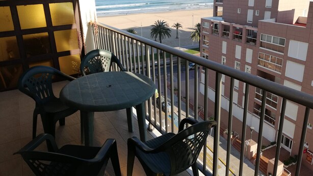 A balcony with a table and chairs overlooking a beach and a cityscape. - Infante E8-7º Solo Familias! (Playa de Gandía)