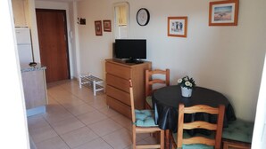 A compact living space with a kitchenette, a dining area with a table and chairs, and a television on a wooden cabinet. - Infante E8-7º Solo Familias! (Playa de Gandía)