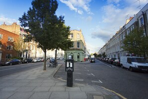 A street with parked cars, a row of terraced houses, and a green building with a sign. - Chelsea Italian Design Home with Terrace (London)