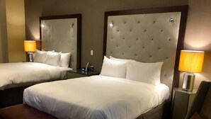 Ein Hotelzimmer mit zwei Betten, jeweils mit einem gepolsterten Kopfteil, einem Nachttisch mit Lampe und einer Sitzbank.