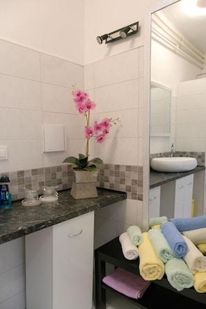 A bathroom with a white sink, a mirror, a potted orchid, and neatly folded towels on a shelf. - Oval Main Square Apartment (Zagreb)